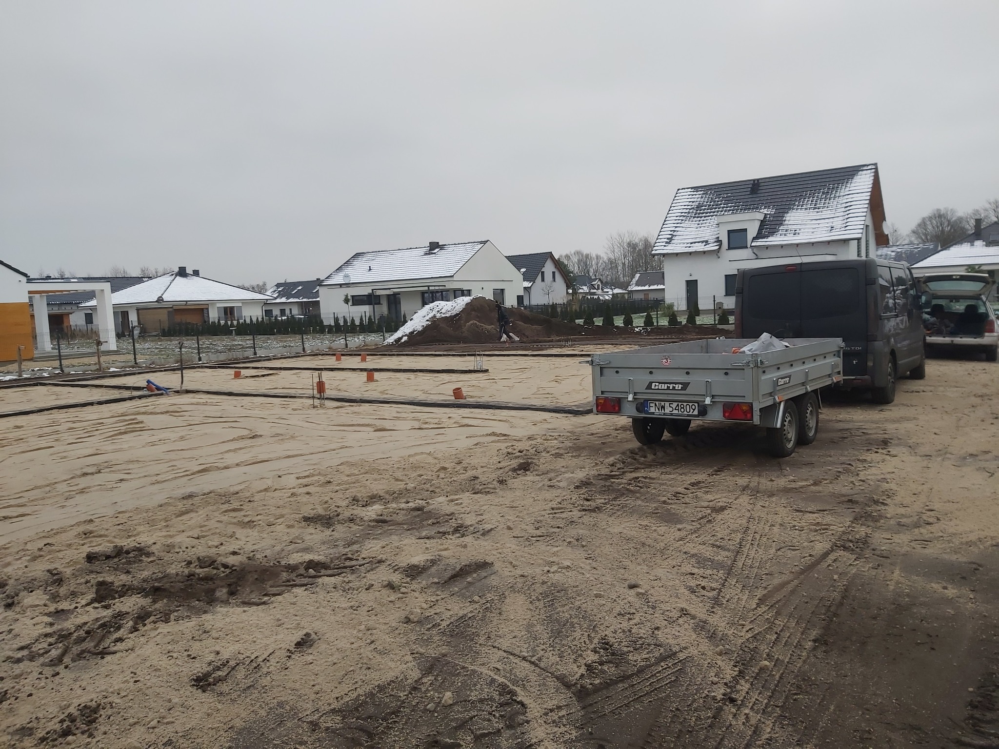 Przygotowanie terenu pod budowę domów jednorodzinnych w Otyniu, widoczny wytyczony plan fundamentów, przyczepa i samochody dostawcze na działce.