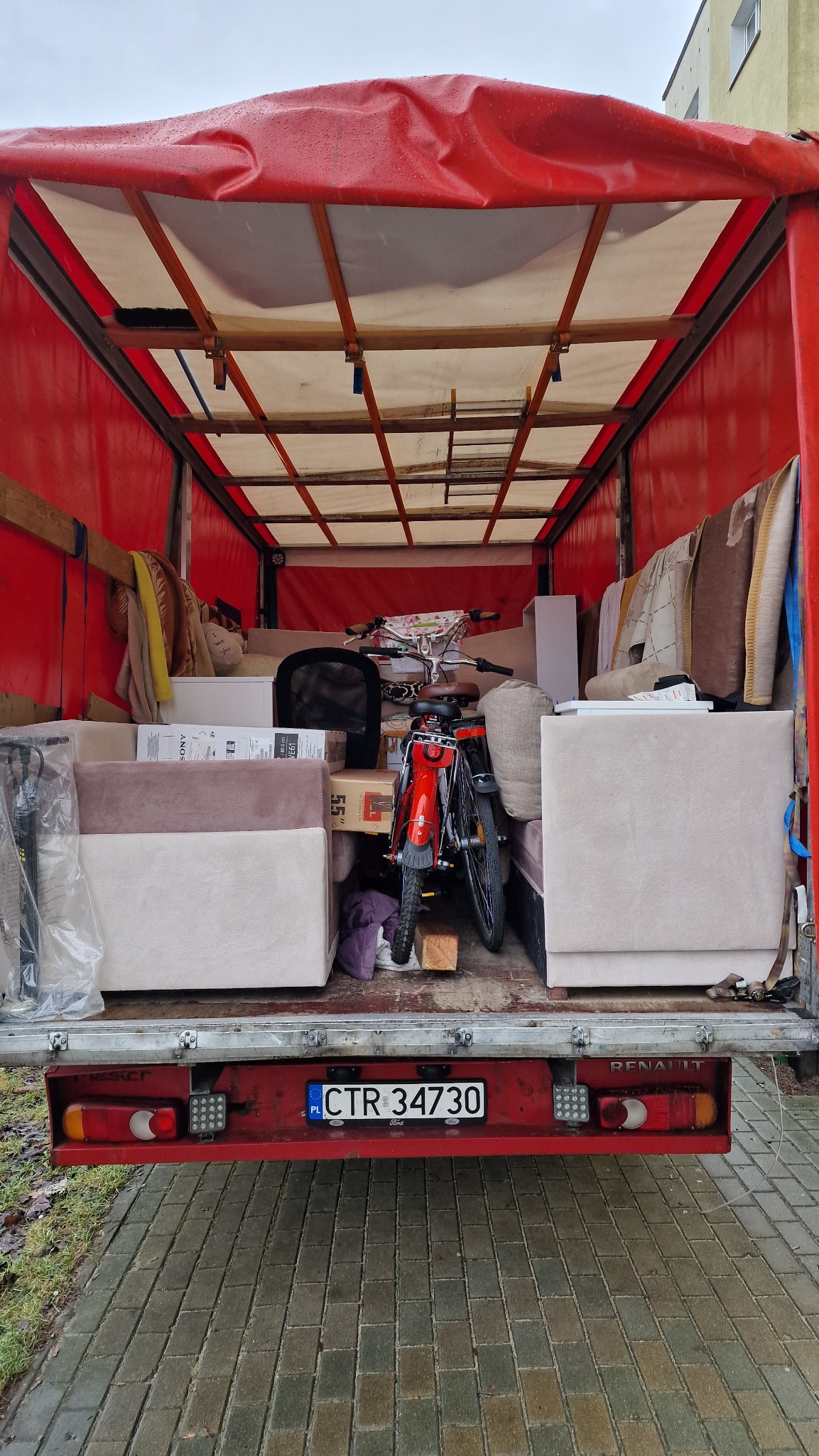 Wnętrze skrzyni ładunkowej czerwonego samochodu dostawczego typu Renault z widocznym rowerem i meblami gotowymi do transportu, tablica rejestracyjna CTR 34730.