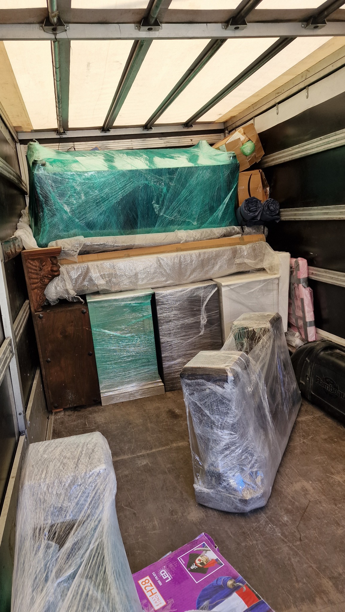 Wnętrze furgonetki załadowane meblami zabezpieczonymi folią stretch przed transportem, widoczny fragment kartonu ze świąteczną dekoracją.