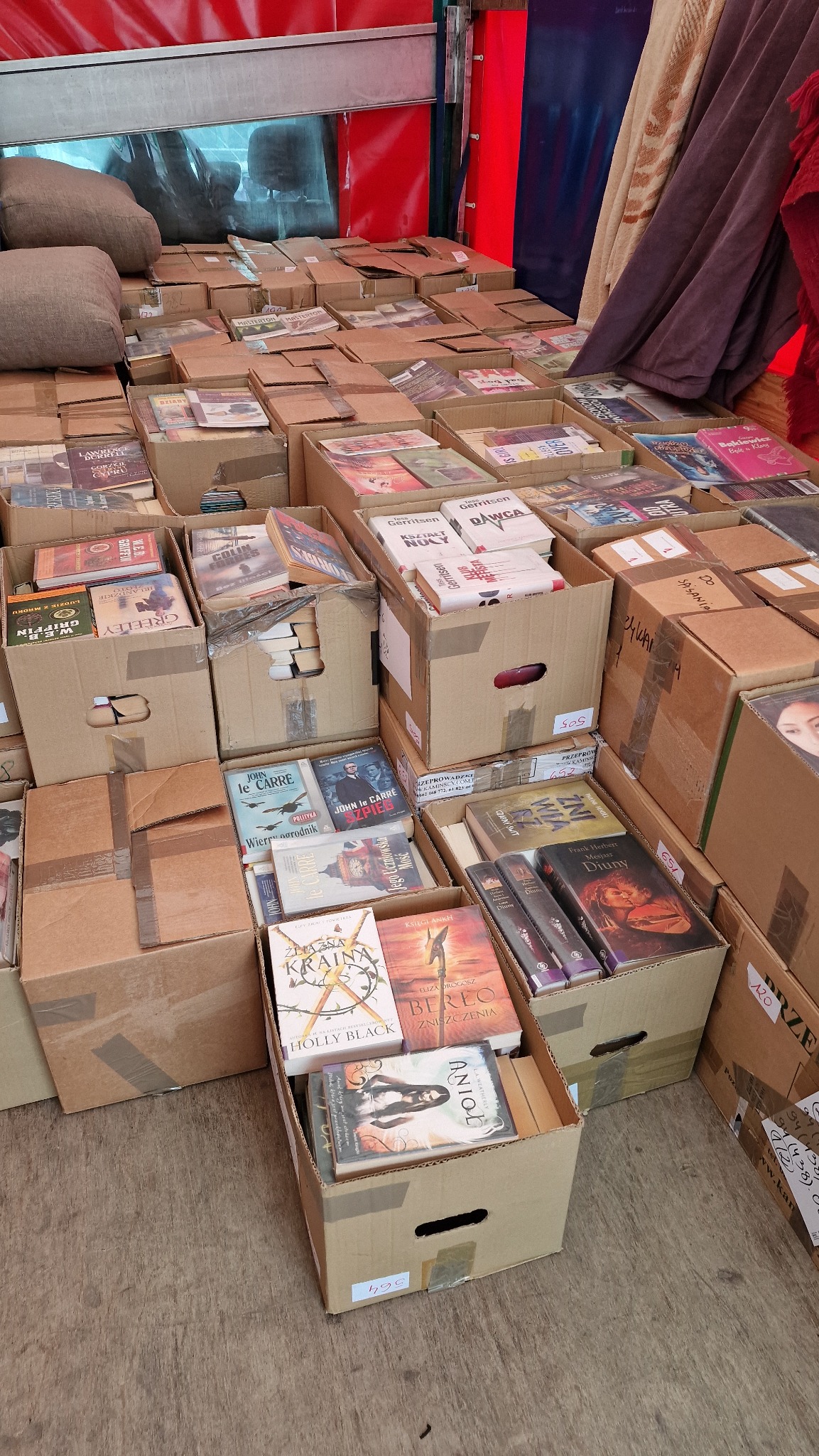 Kilkadziesiąt kartonowych pudeł wypełnionych książkami, przygotowanych do transportu, widocznych pod zadaszeniem.