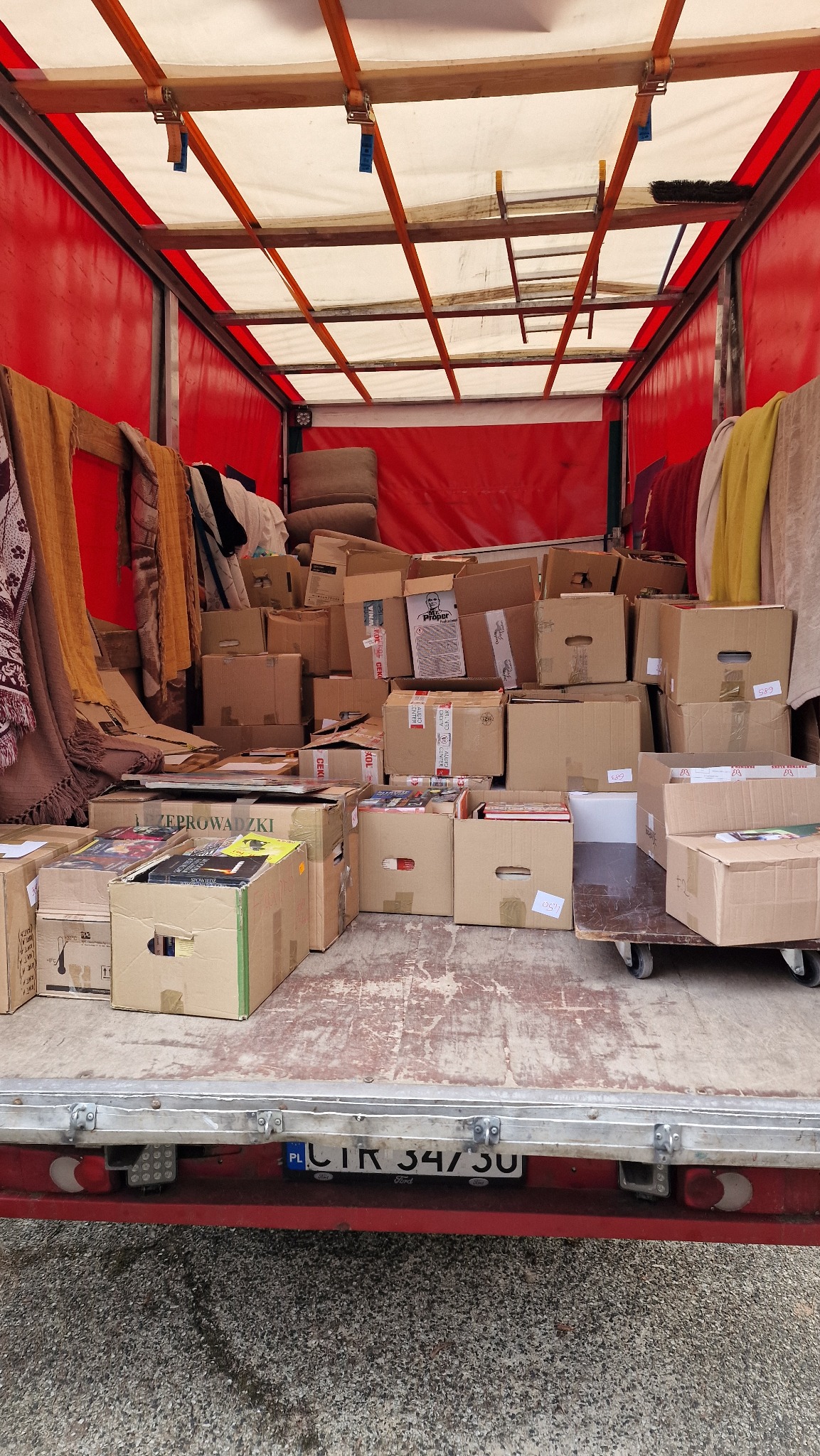 Wnętrze busa transportowego załadowane kartonami z rzeczami podczas przeprowadzki, widoczna tablica rejestracyjna PL.