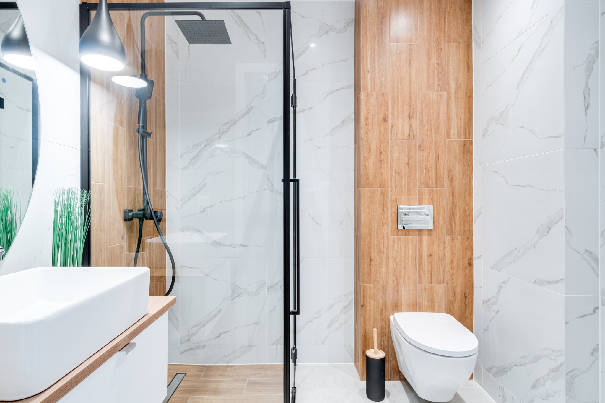 Nowoczesna łazienka z kabiną prysznicową typu walk-in z czarnymi ramami, umywalką nablatową, drewnopodobnymi i marmurowymi płytkami na ścianach oraz podwieszaną toaletą.