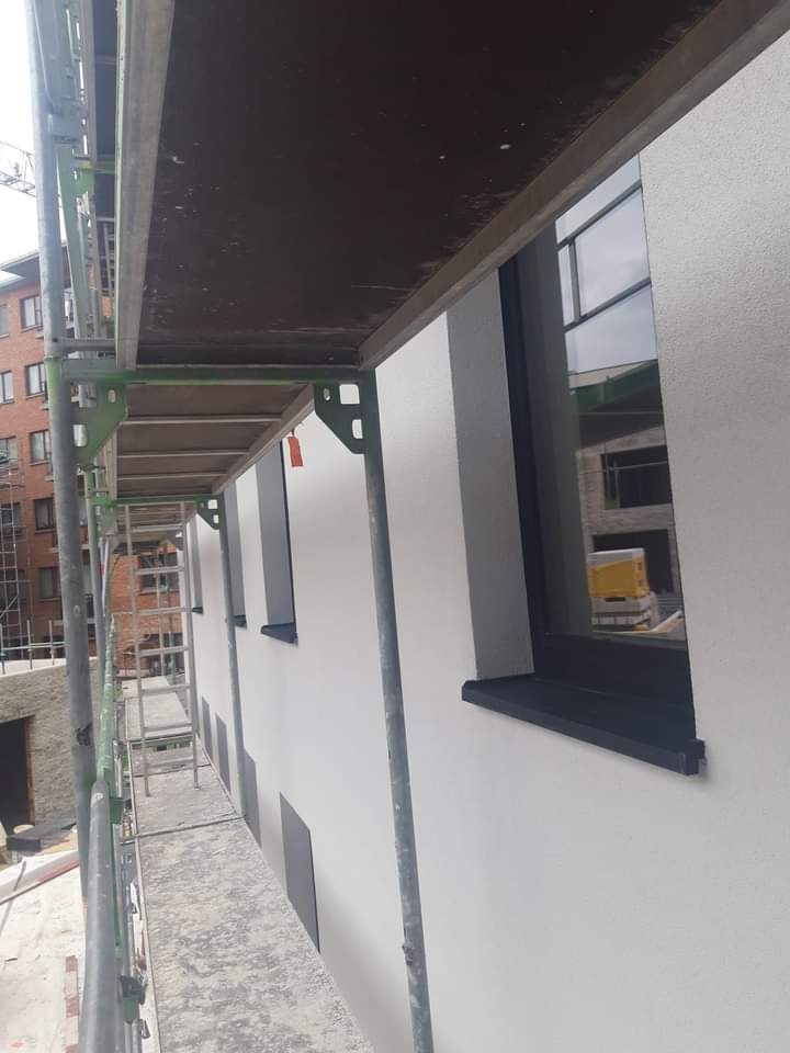 Elewacja budynku w trakcie ocieplania, widoczne rusztowanie, okna z czarnymi parapetami i fragmenty ocieplenia na ścianie.