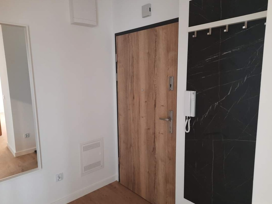 Nowoczesny przedpokój z drewnianymi drzwiami wejściowymi, czarną ścianą z marmurowym wzorem i lustrem po lewej stronie.