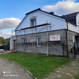 Dom jednorodzinny w trakcie ocieplania, widoczne rusztowania, styropian na elewacji, częściowo otynkowane okna, numer domu 241.