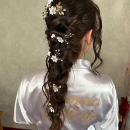 ZmalowAna by Anna Prażmo - Upięcie ślubne z warkoczem i kwiatowymi ozdobami, widok z tyłu, na ramionach biały szlafrok z napisem 'Panna Młoda'.