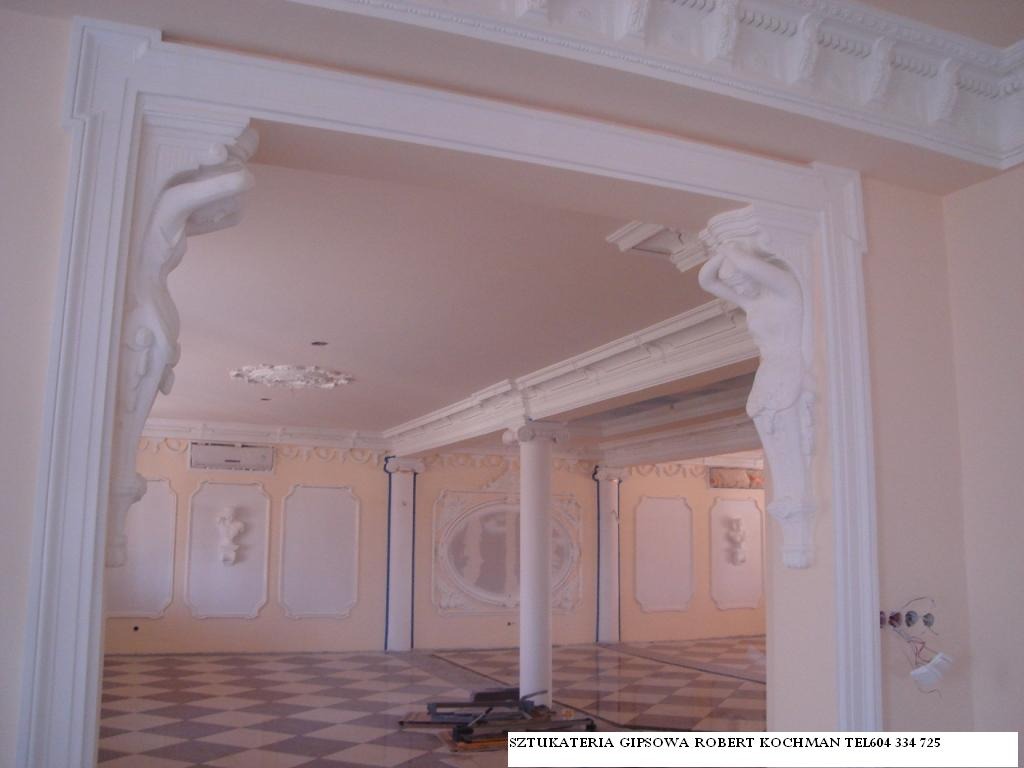 Wykończone wnętrze z dekoracyjną sztukaterią gipsową: kolumny, listwy przysufitowe i płaskorzeźby na ścianach, widok przez ozdobny portal z figurami. Podłoga w szachownicę.