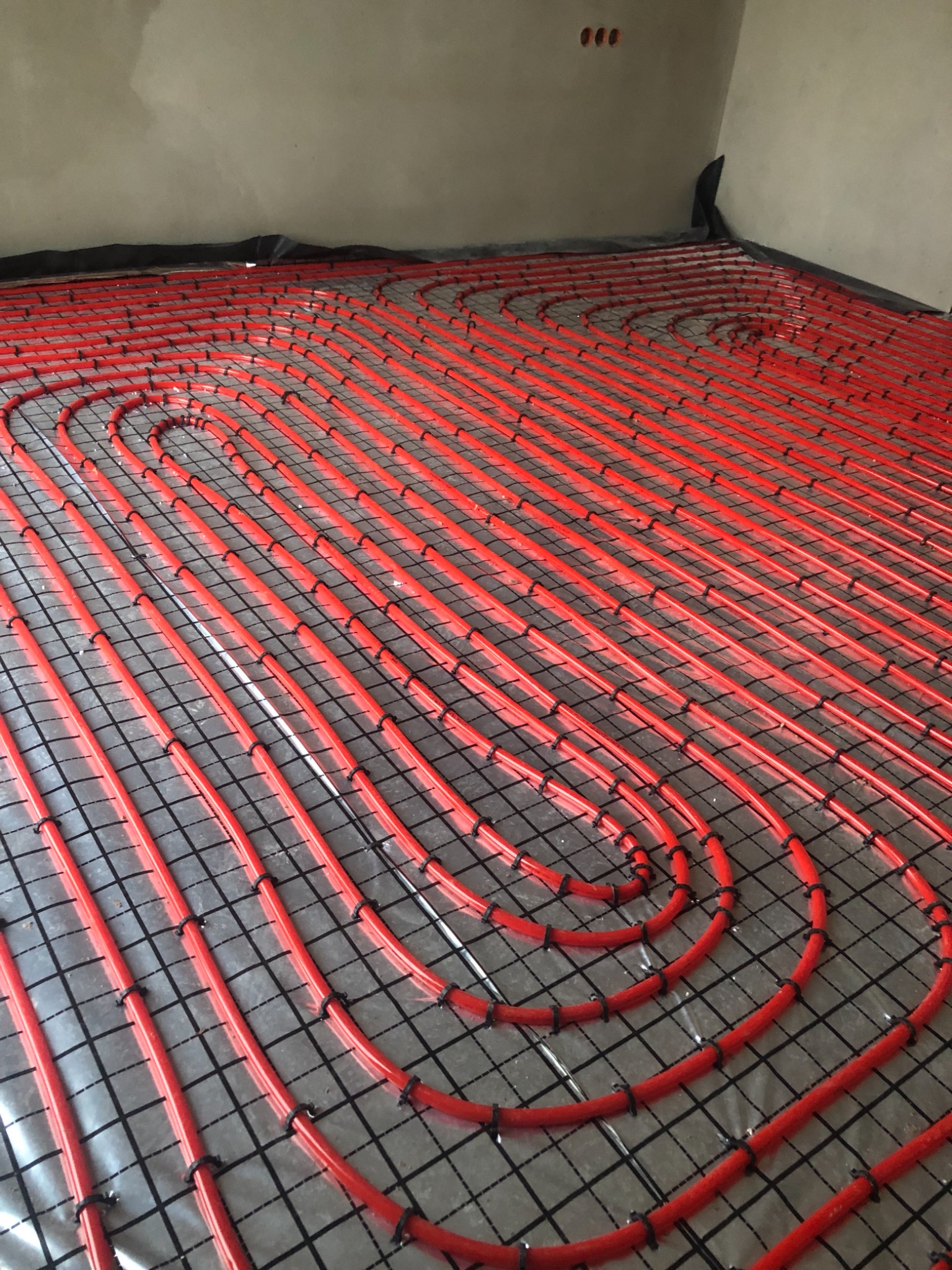 Czerwone rury ogrzewania podłogowego ułożone na czarnej siatce w surowym wnętrzu, widok z góry pod kątem.