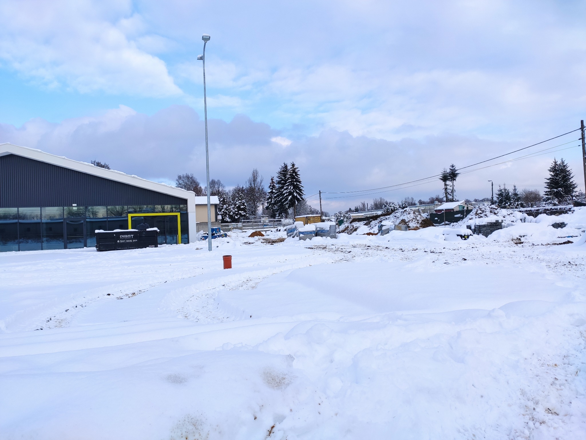 Zimowy krajobraz placu budowy po inwentaryzacji, z budynkiem w tle i stertami śniegu na pierwszym planie.