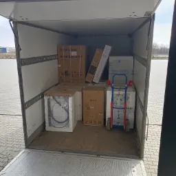 Wnętrze przestrzeni ładunkowej busa wypełnione kartonami z nowym sprzętem AGD i RTV, w tym lod&oacute;wka Samsung, pralka i telewizor LG OLED, zabezpieczonymi w&oacute;zkami transportowymi.