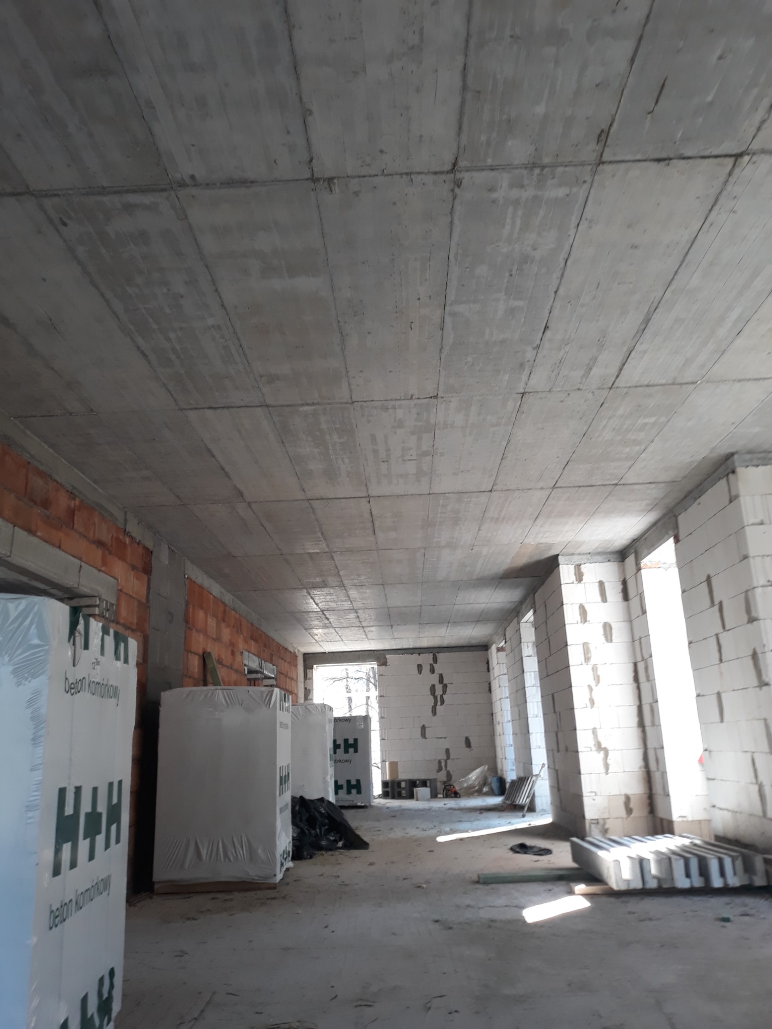 Surowy strop żelbetowy w budynku w stanie surowym otwartym, widoczne ściany z betonu komórkowego i cegły, opakowania bloczków H+H.
