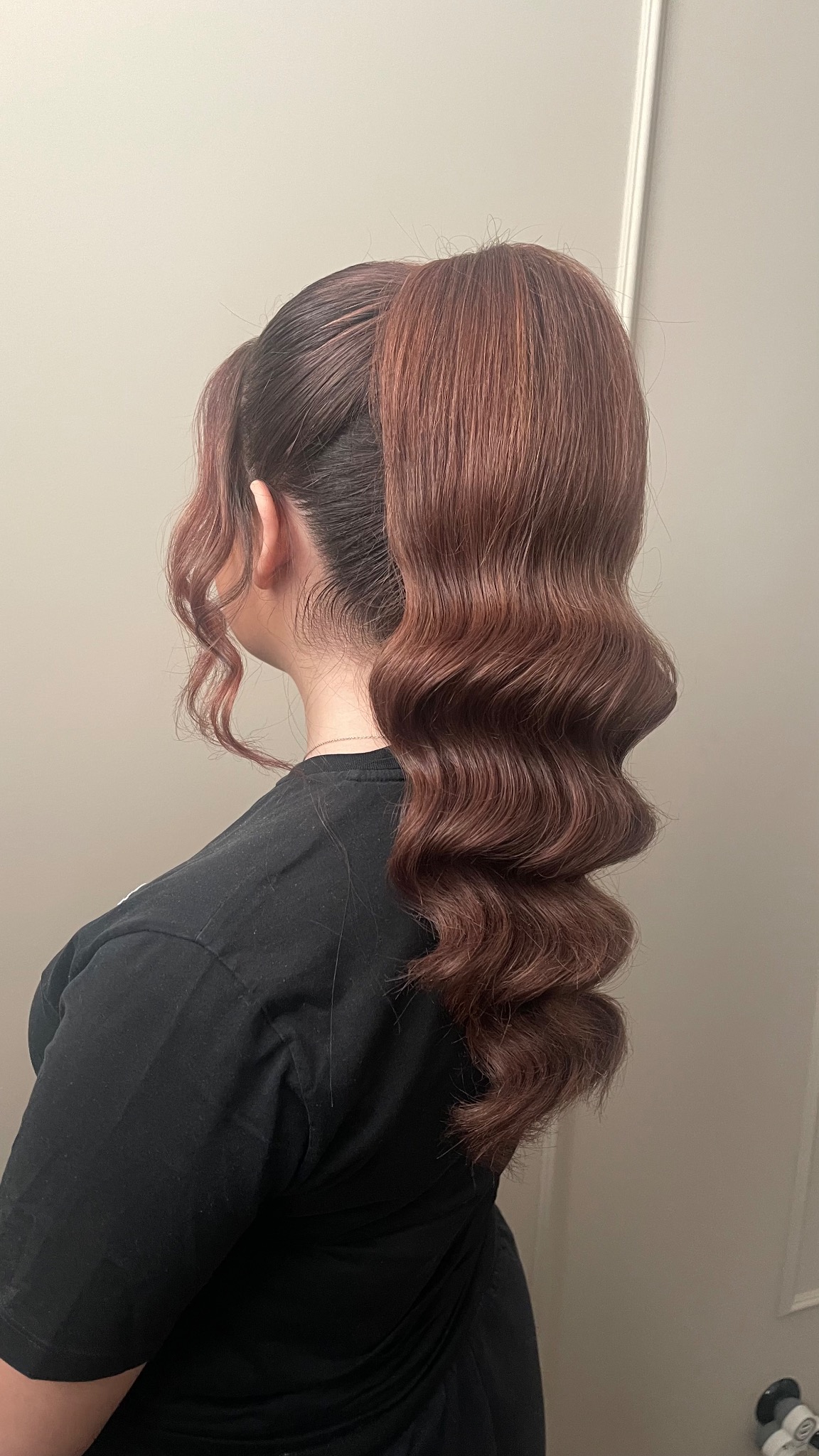 Kobieta z tyłu głowy, prezentująca brązowe włosy upięte w wysoki kucyk z wyraźnymi falami w stylu retro, delikatne kosmyki opadają przy uszach.