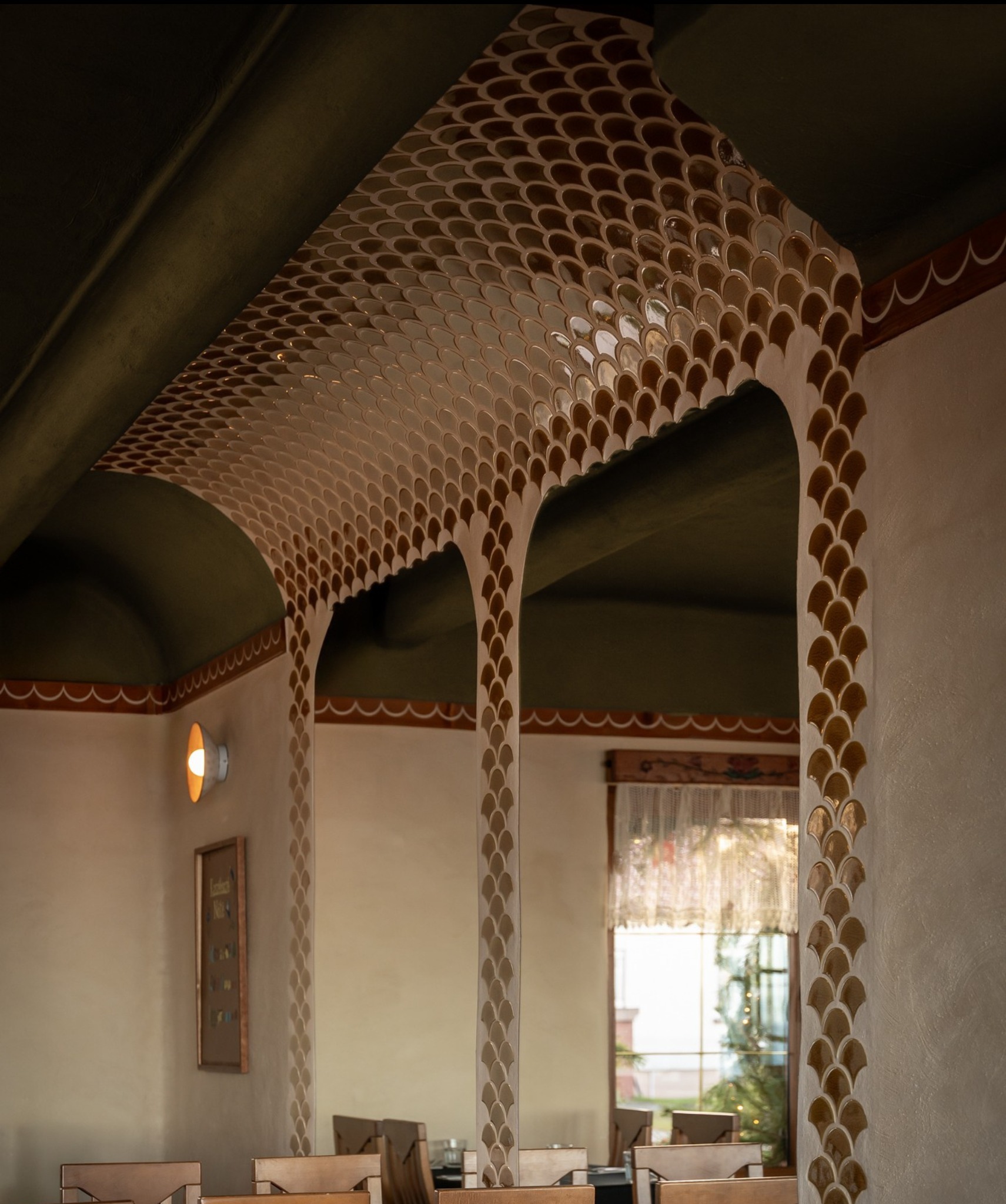 Dekoracyjny łuk z mozaiką w kształcie rybich łusek, zdobiący przejście w restauracji. Ciepłe oświetlenie i subtelne zdobienia ścian tworzą unikalny klimat wnętrza.