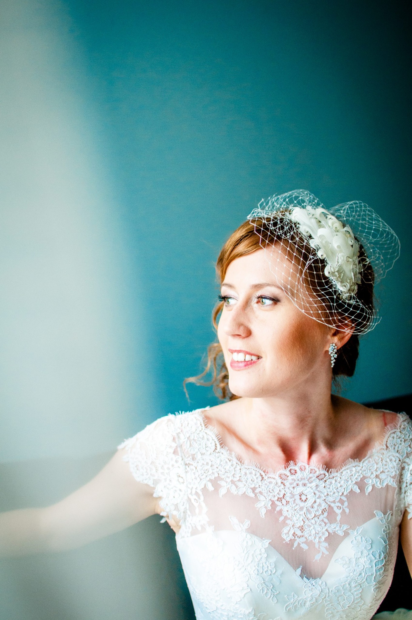 Panna młoda w Szczecinie, w koronkowej sukni i toczku z woalką, patrzy w lewo, na tle błękitnej ściany.