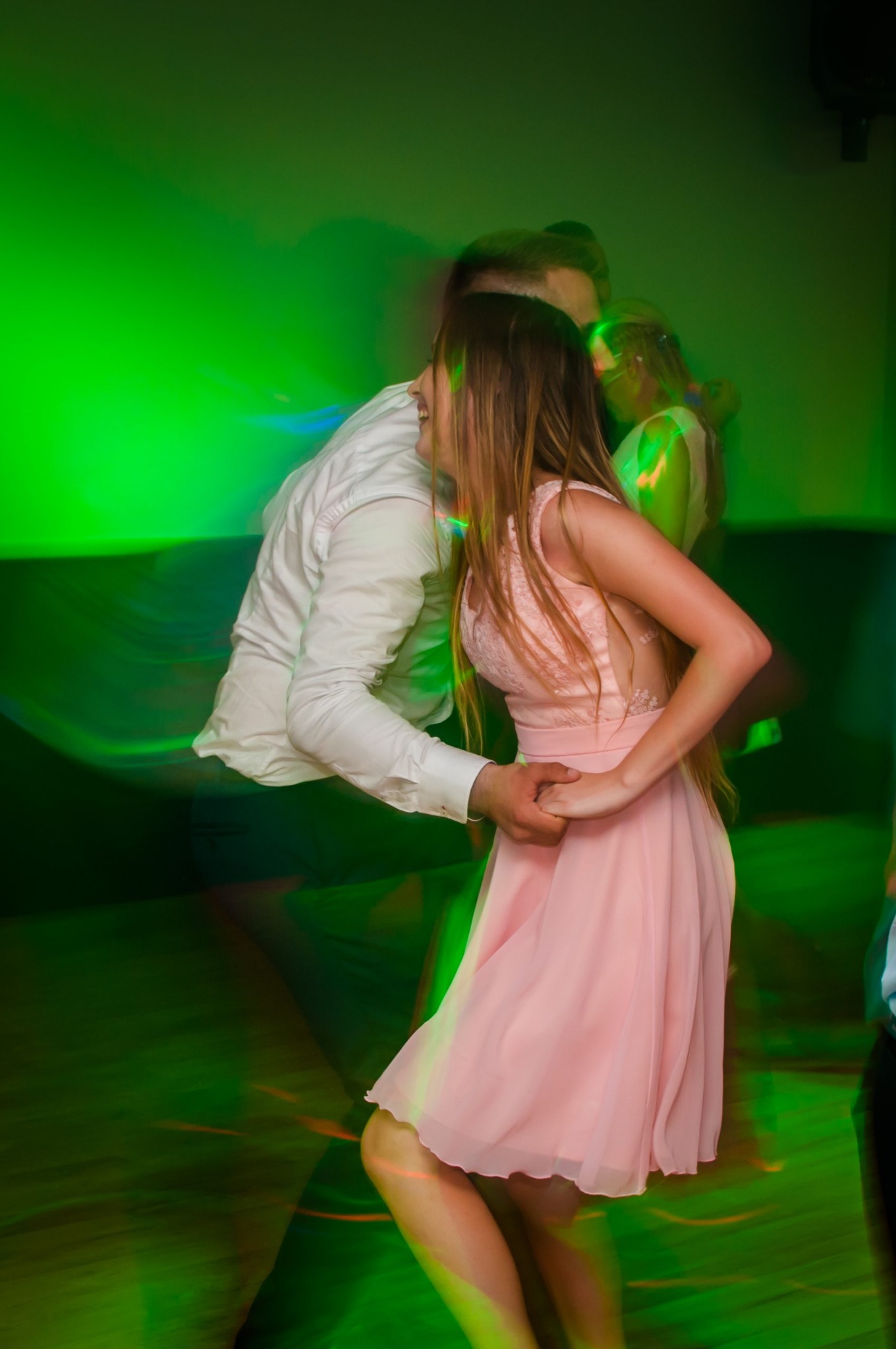 Para tańcząca na parkiecie w zielonym oświetleniu, dziewczyna w różowej sukience z koronką, mężczyzna w białej koszuli, dynamiczne ujęcie z rozmytym tłem.