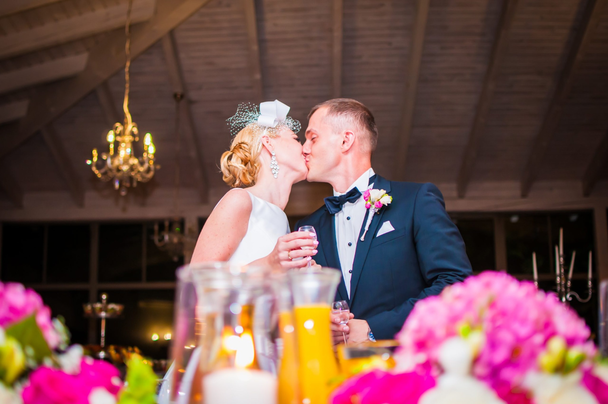 Pocałunek nowożeńców w eleganckiej sali weselnej z kryształowym żyrandolem, dekoracje kwiatowe i świece na pierwszym planie.