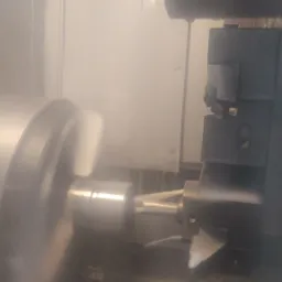 Metalowy element obrabiany wewnątrz maszyny CNC, widoczne chłodziwo i wirujące narzędzie skrawające.