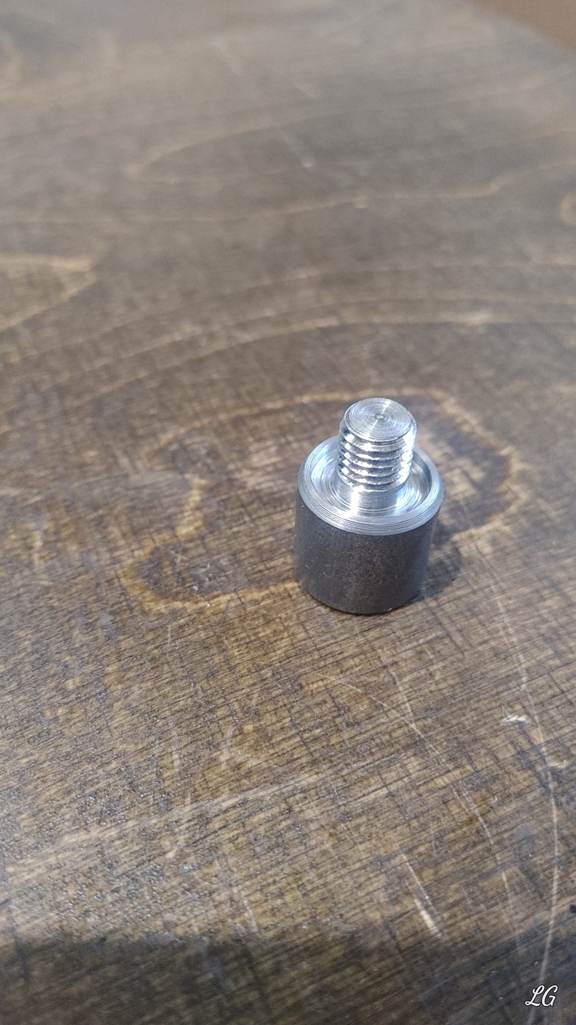 Metalowy element z gwintem na drewnianym blacie, prawdopodobnie wykonany na tokarce lub obrabiarce CNC, widoczne ślady obróbki.