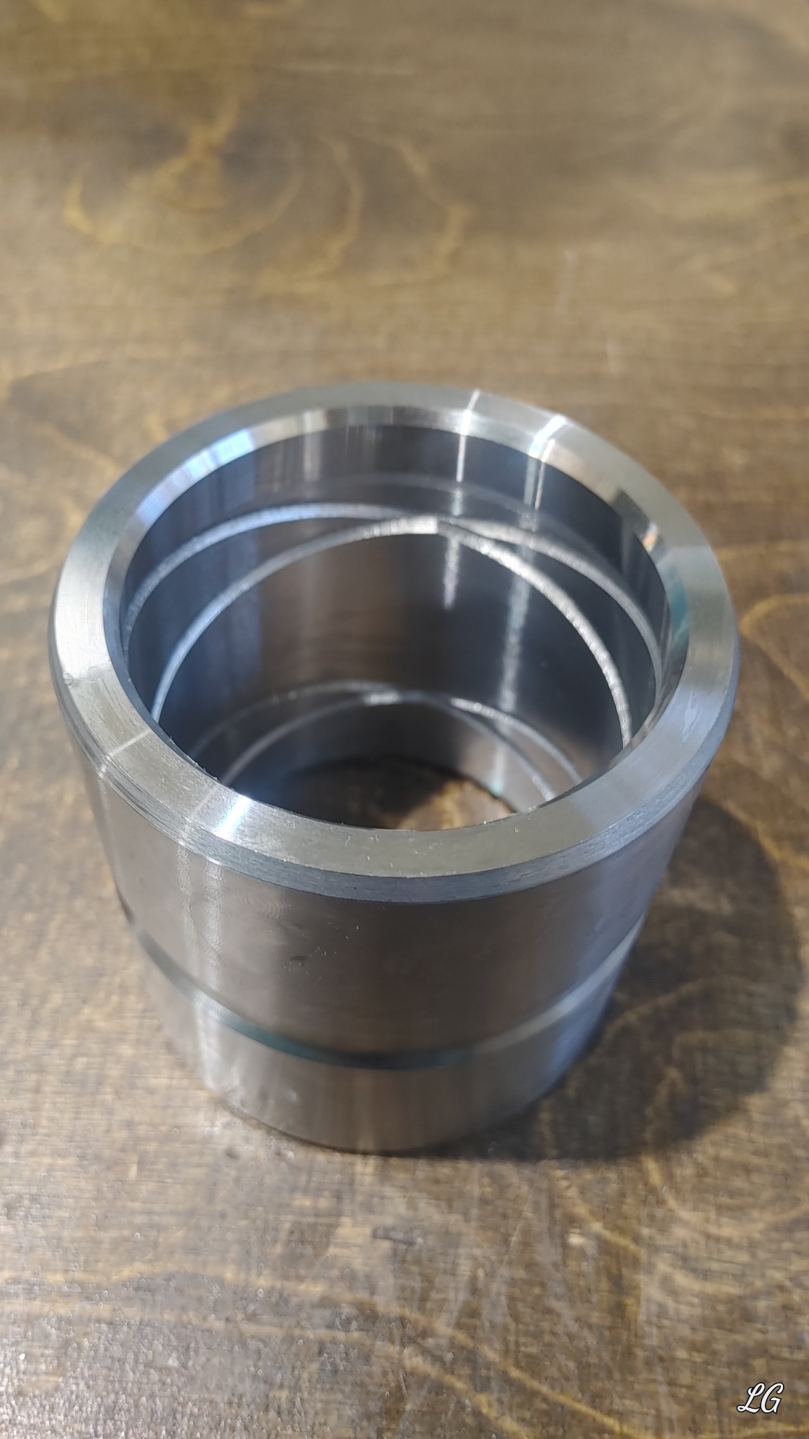 Metalowy pierścień z wewnętrznymi rowkami, obrobiony i ułożony na drewnianym blacie, widoczne ślady obróbki.