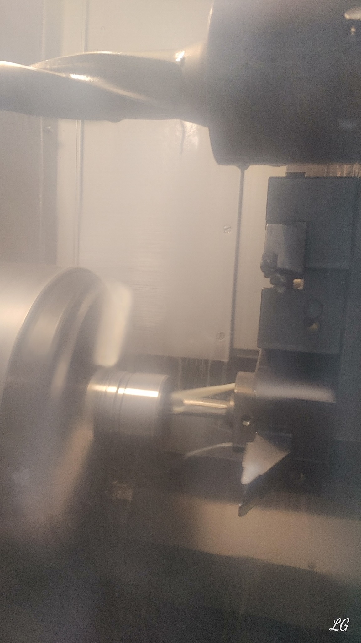 Metalowy element obrabiany wewnątrz maszyny CNC, widoczne chłodziwo i wirujące narzędzie skrawające.