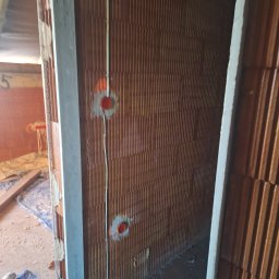 SZM HOLDING SPÓŁKA Z OGRANICZONĄ ODPOWIEDZIALNOŚCIĄ - Instalacja elektryczna w trakcie montażu: przewody i puszki w ścianie z cegły dziurawki. Widoczne elementy instalacji w surowym stanie.