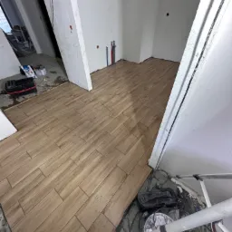 Ułożone panele podłogowe imitujące drewno w trakcie remontu, widoczne narzędzia i niedokończone ściany.