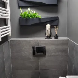 Nowoczesna łazienka w odcieniach szarości z wiszącą toaletą, dekoracyjnymi donicami z roślinami i grzejnikiem drabinkowym.