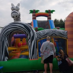 P.W. Mieczysław Grzeszczuk - Duży, dmuchany zamek w kształcie zebry i dżungli, z dwoma osobami dorosłymi w pobliżu, ustawiony na trawie obok wzorzystego dywanu.