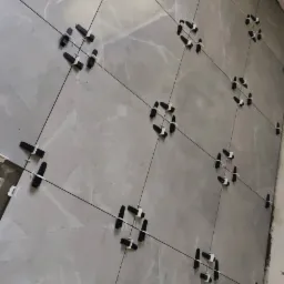 Montaż szarych płytek ściennych z użyciem systemu poziomowania, widoczne czarne kliny i cienkie sznurki tworzące siatkę.