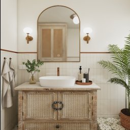 Emilia Wróbel Design - Jasna łazienka z umywalką na szafce z plecionki, lustrem w złotej ramie i rośliną w doniczce. Wnętrze w stylu boho z wzorzystą podłogą.