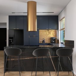 Emilia Wróbel Design - Nowoczesna kuchnia w ciemnej kolorystyce z marmurowym blatem, złotym okapem cylindrycznym i drewnianą podłogą w jodełkę. Minimalistyczny design.