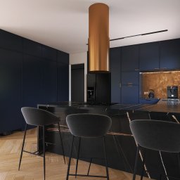 Emilia Wróbel Design - Ekskluzywna kuchnia: granatowe szafki, marmurowa wyspa z hokerami, miedziany okap cylindryczny. Parkiet w jodełkę i robot sprzątający w tle.