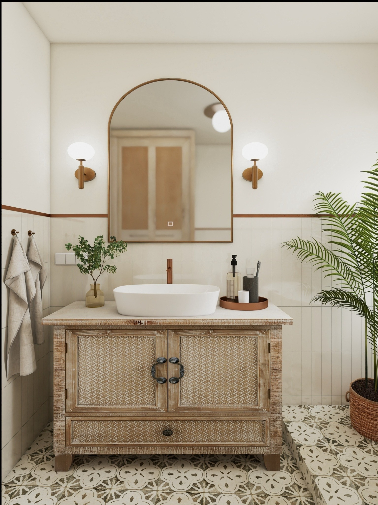 Jasna łazienka z umywalką na szafce z plecionki, lustrem w złotej ramie i rośliną w doniczce. Wnętrze w stylu boho z wzorzystą podłogą.