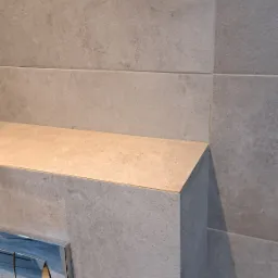 Szare, matowe płytki w łazience, zabudowa stelaża WC z chromowanym przyciskiem spłukującym.