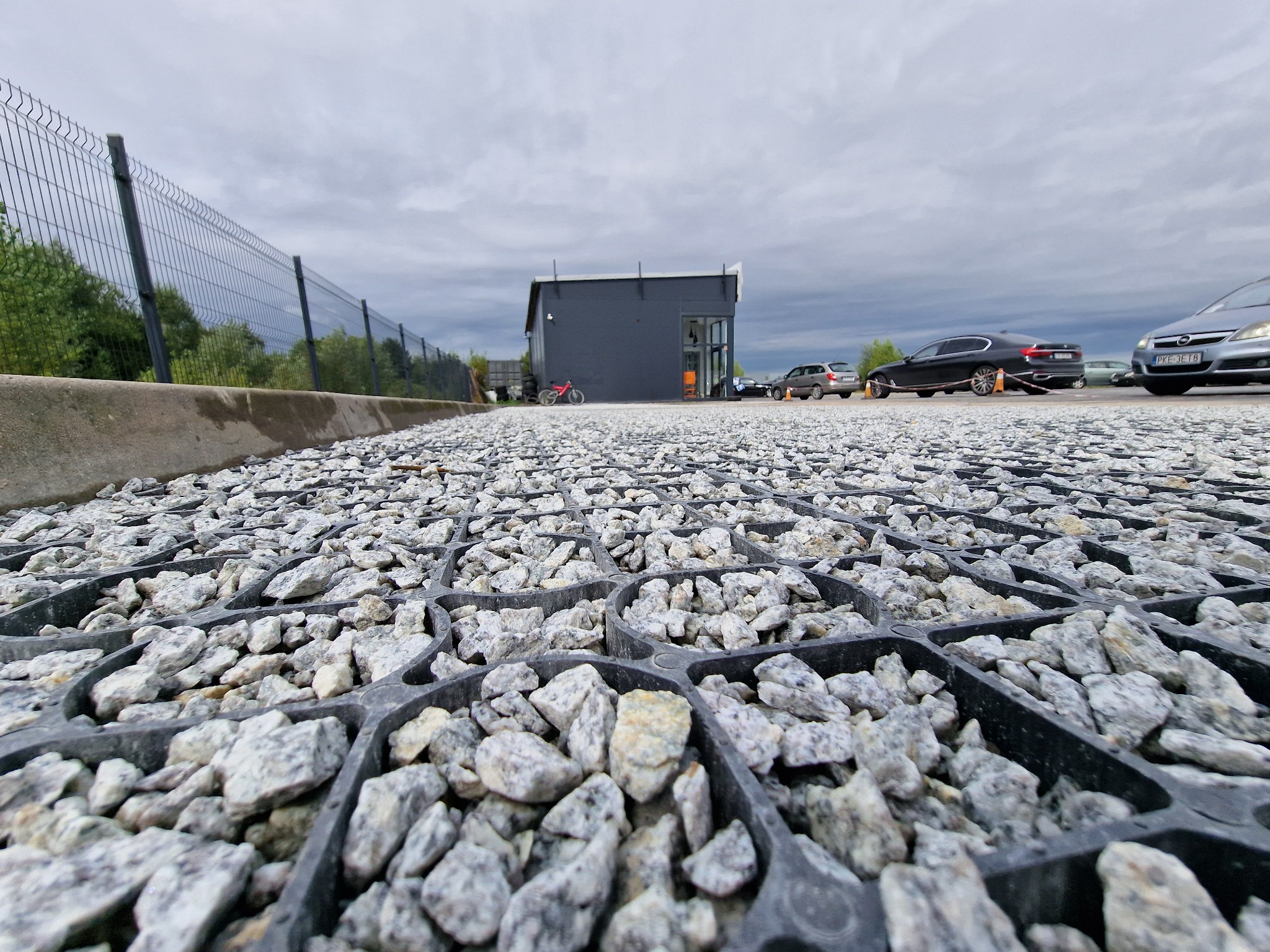 Utwardzona nawierzchnia z kruszywa w plastikowych kratkach, widok z poziomu gruntu, budynek w tle, samochody zaparkowane obok