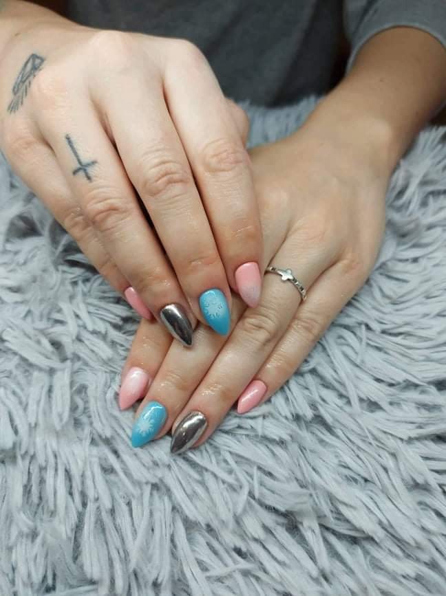 Dłonie z pomalowanymi paznokciami w kolorach pastelowego różu, błękitu z białymi płatkami śniegu i metalicznego srebra, na tle puszystego dywanu.