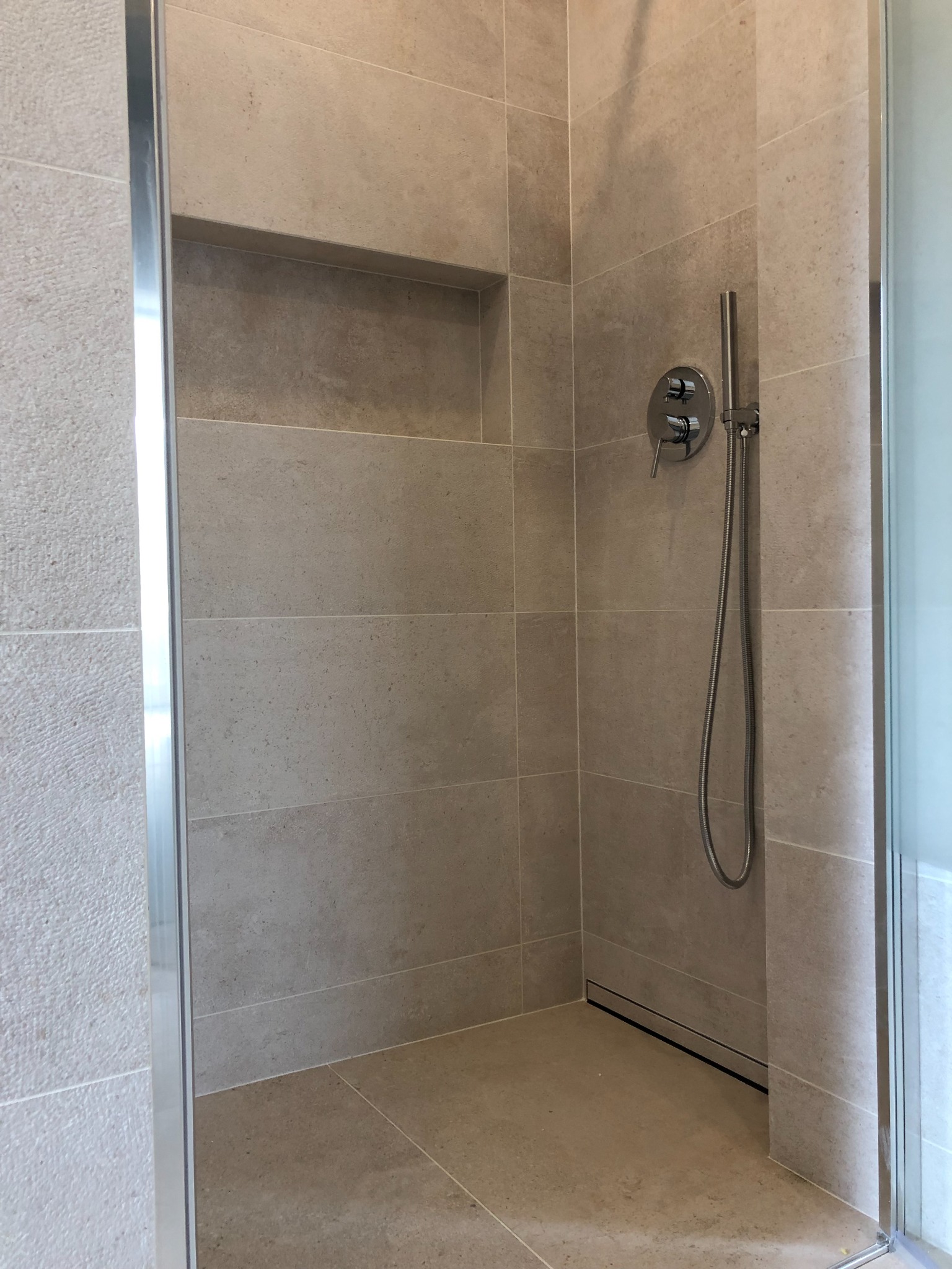 Beżowa kabina prysznicowa z wnęką ścienną, chromowaną armaturą i odpływem liniowym