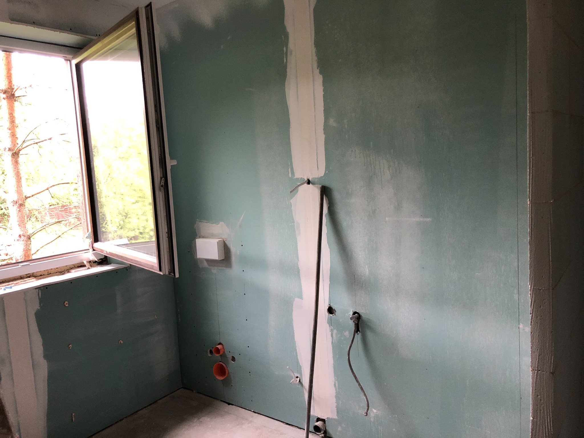 Ściana z płyt gipsowo-kartonowych w trakcie szpachlowania w Łodzi, widoczne otwory na instalacje oraz częściowo otwarte okno.