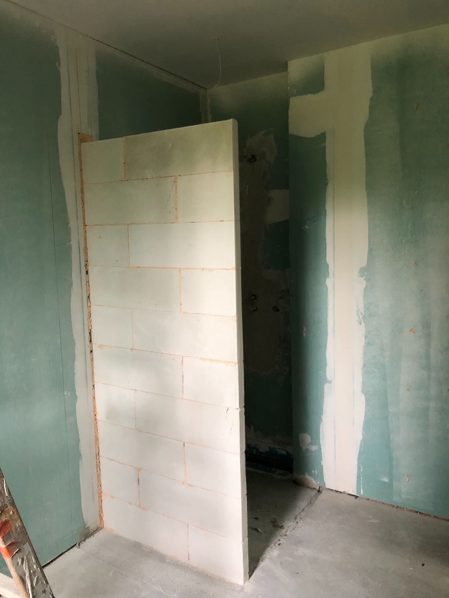 Wnętrze w trakcie remontu: murowana ścianka działowa z bloczków, surowe ściany z widocznymi śladami szpachlowania i pionowe pasy świeżo położonej gładzi.
