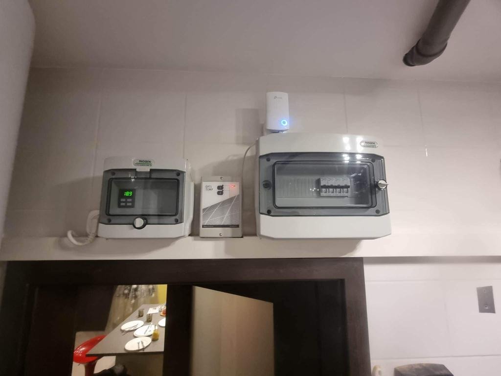 Rozdzielnice elektryczne NOARK i moduł Opti-Temp zamontowane na kafelkowanej ścianie nad drzwiami, widoczny fragment instalacji rurowej pod sufitem.