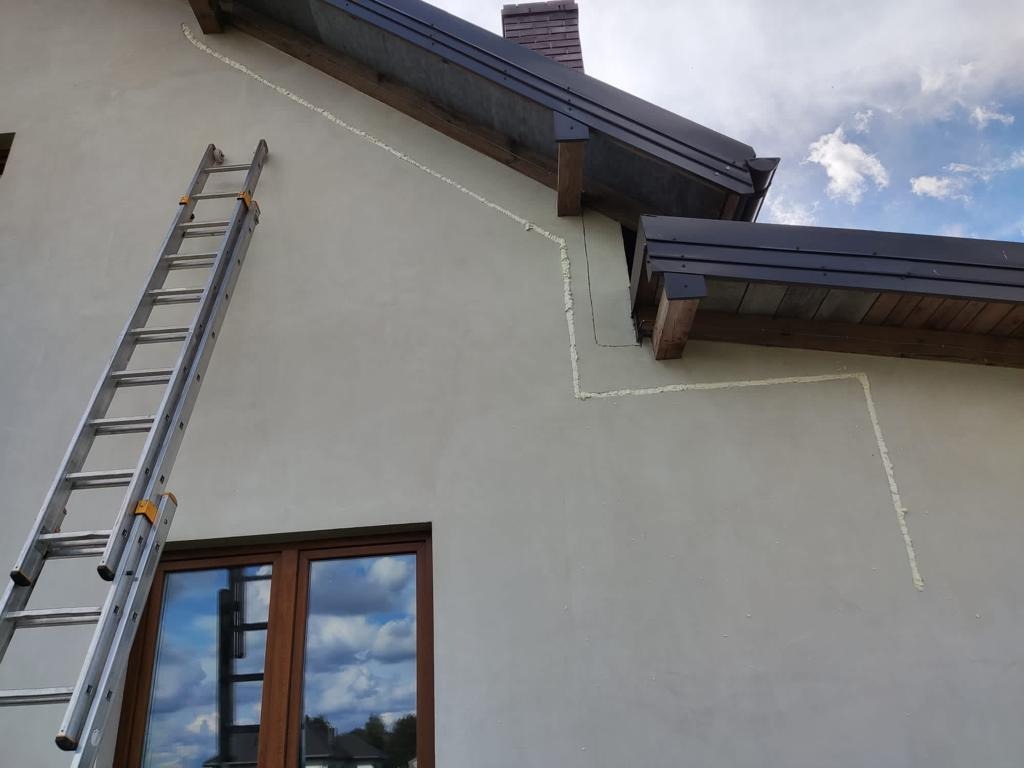 Elewacja budynku z widocznymi śladami po montażu instalacji, zabezpieczona pianką montażową, drabina oparta o ścianę przy oknie.