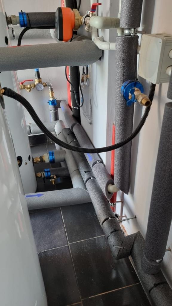 Węzeł instalacyjny z rurami w izolacji termicznej, zaworami i manometrami, zamontowany w kotłowni w Jaworznie. Widoczne elementy instalacji grzewczej i wodnej.