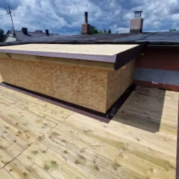 Konstrukcja dachu z desek i płyty OSB w słoneczny dzień. Widoczne kominy na tle nieba z chmurami. Etap prac dekarskich, budowa lukarny.