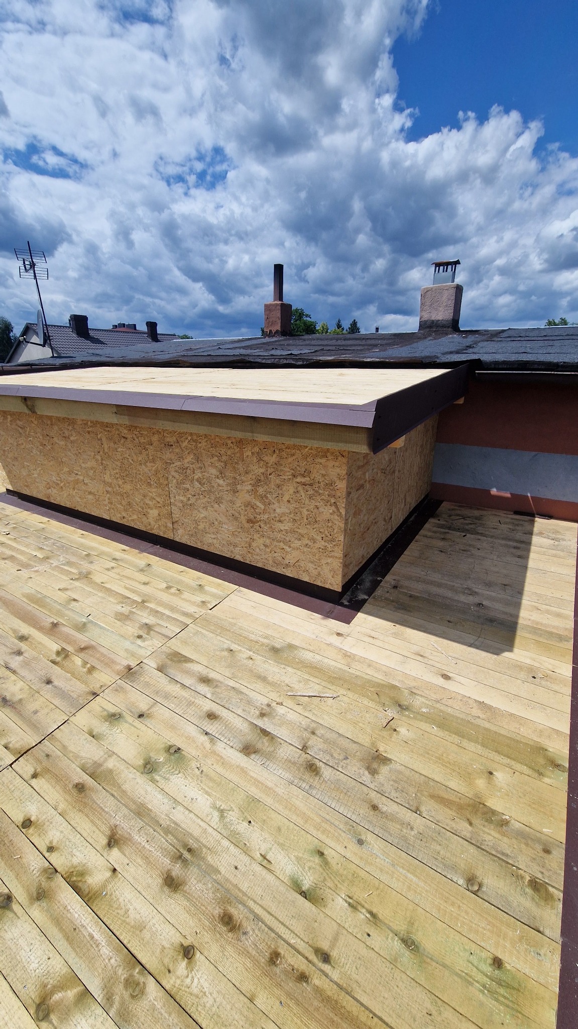 Konstrukcja dachu z desek i płyty OSB w słoneczny dzień. Widoczne kominy na tle nieba z chmurami. Etap prac dekarskich, budowa lukarny.