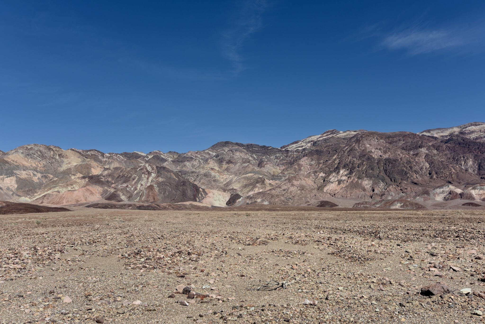 Krajobraz pustynny z górami w tle pod błękitnym niebem, widok na rozległą, kamienistą równinę z wyraźnymi warstwami skalnymi na zboczach gór.
