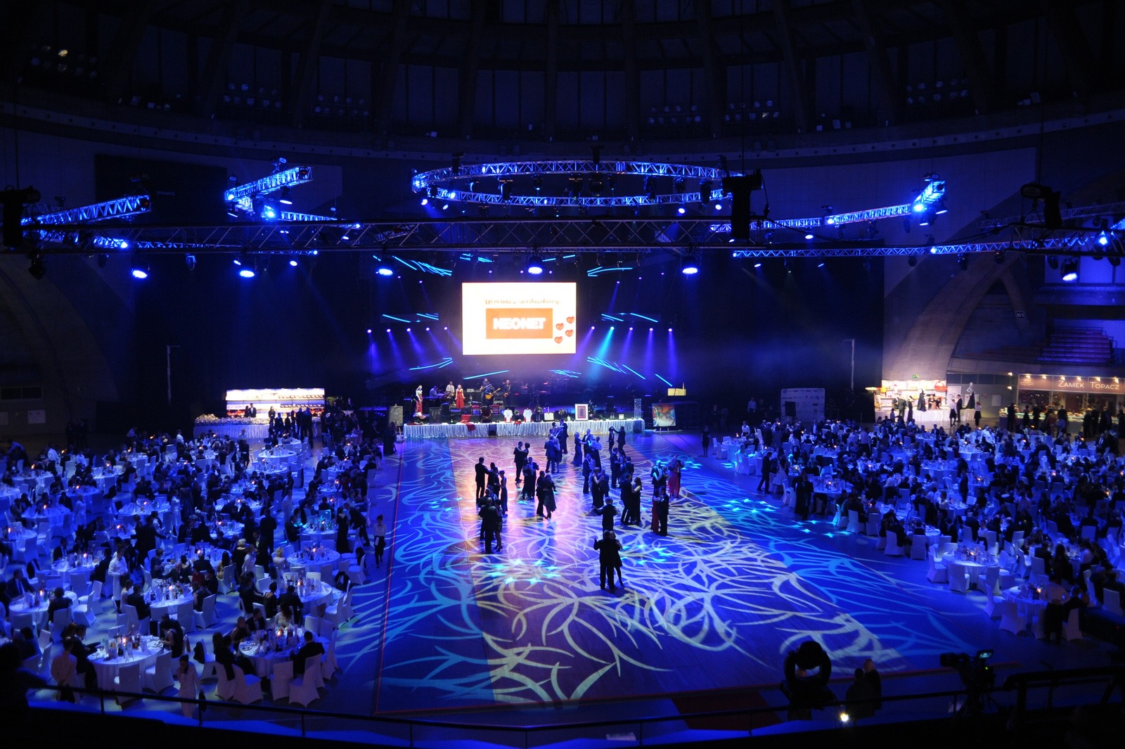 Widok z góry na dużą salę balową z oświetleniem scenicznym, stołami bankietowymi i tańczącymi gośćmi podczas eventu firmowego Neonet.