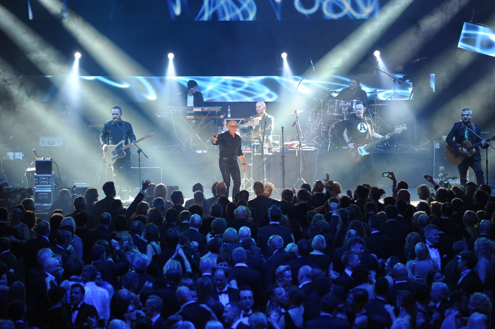 Zespół muzyczny na scenie podczas eventu, oświetlony reflektorami, z widoczną publicznością w dole.