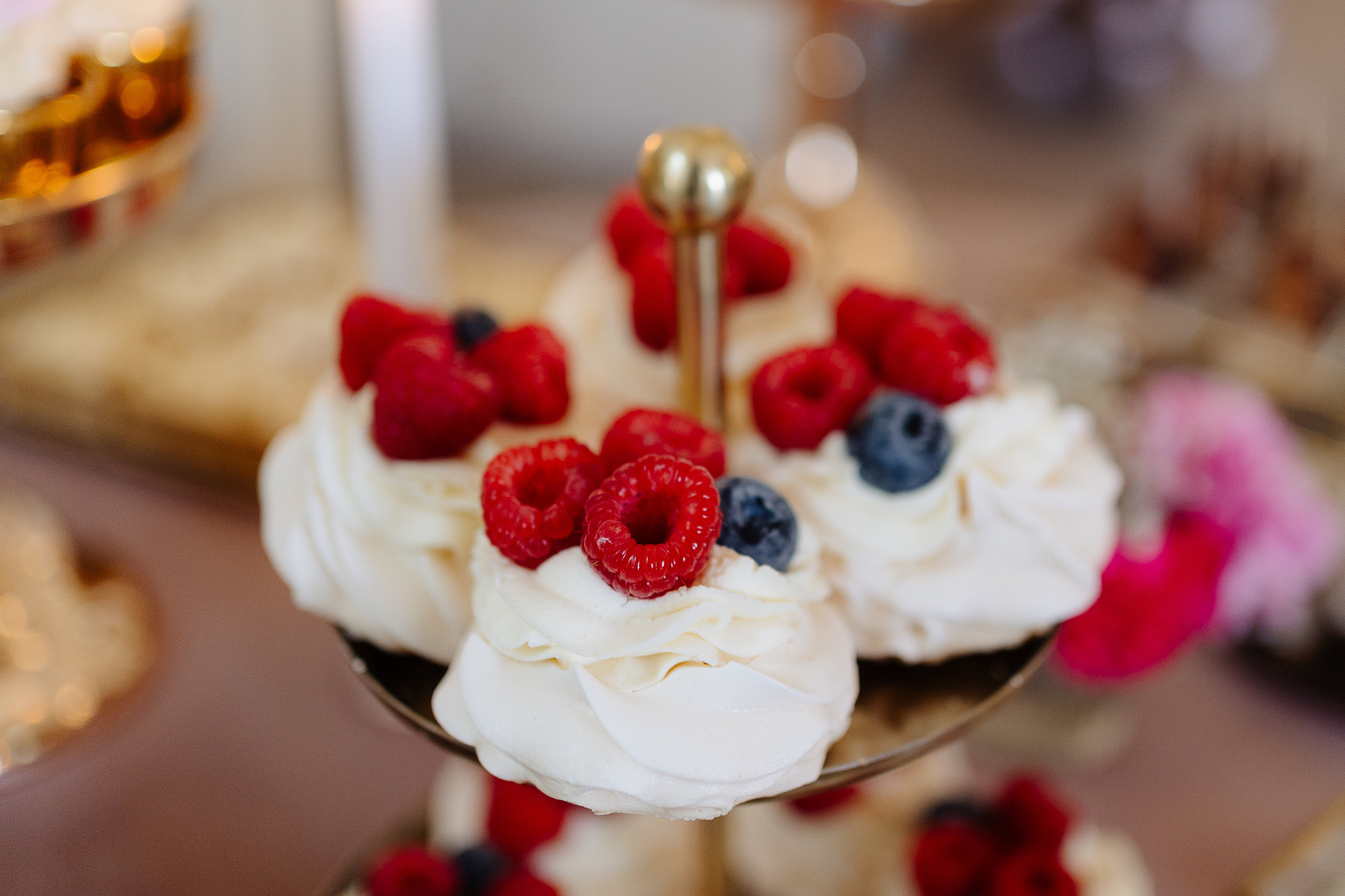 Delikatne mini bezy z malinami i borówkami na eleganckiej, złotej paterze. Słodki deser na przyjęciu okolicznościowym, uchwycony w miękkim, naturalnym świetle.