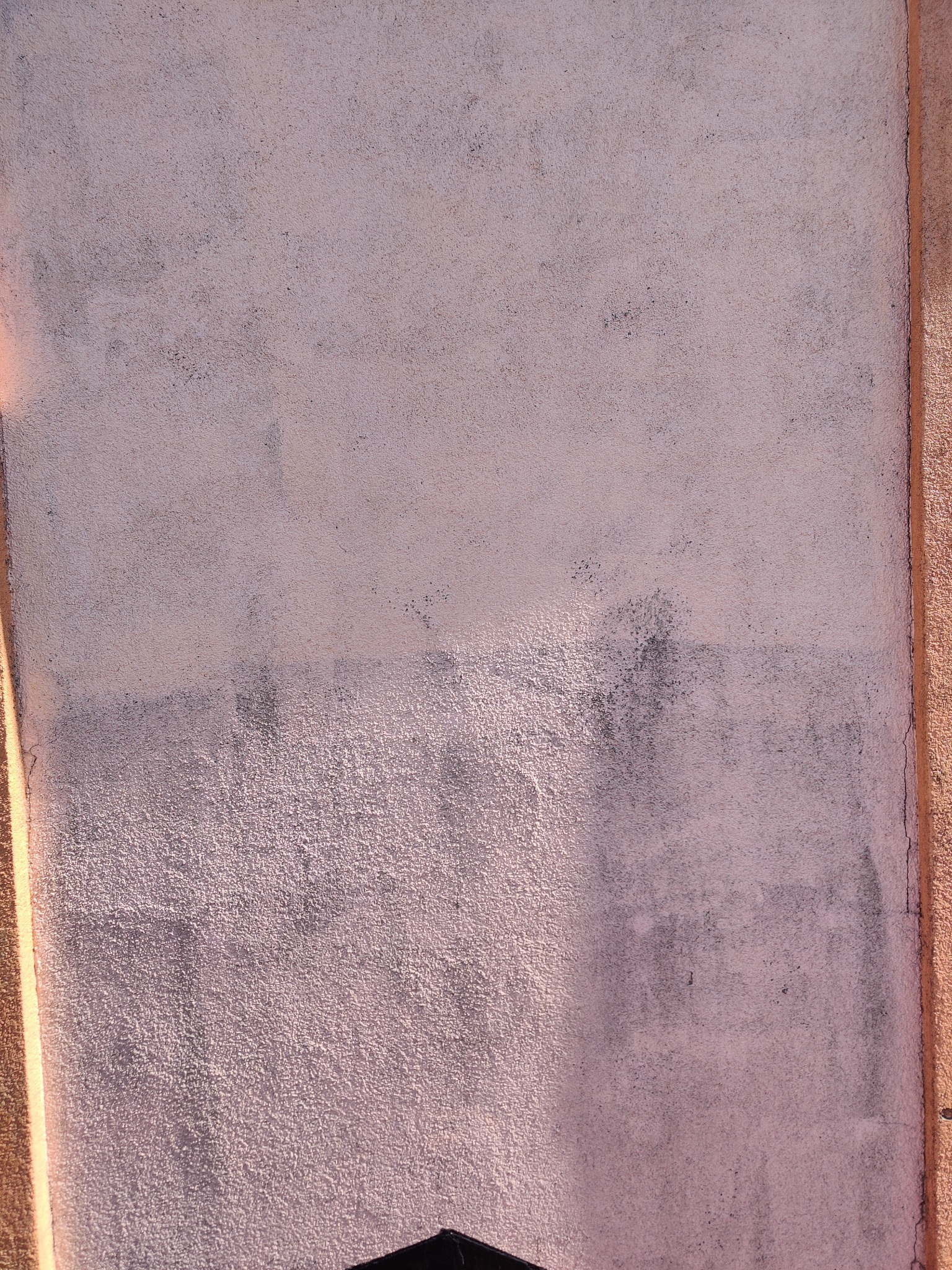 Fragment ściany zewnętrznej z nierównomiernie nałożoną, różową farbą, widoczne ślady zabrudzeń i różnice w odcieniach.