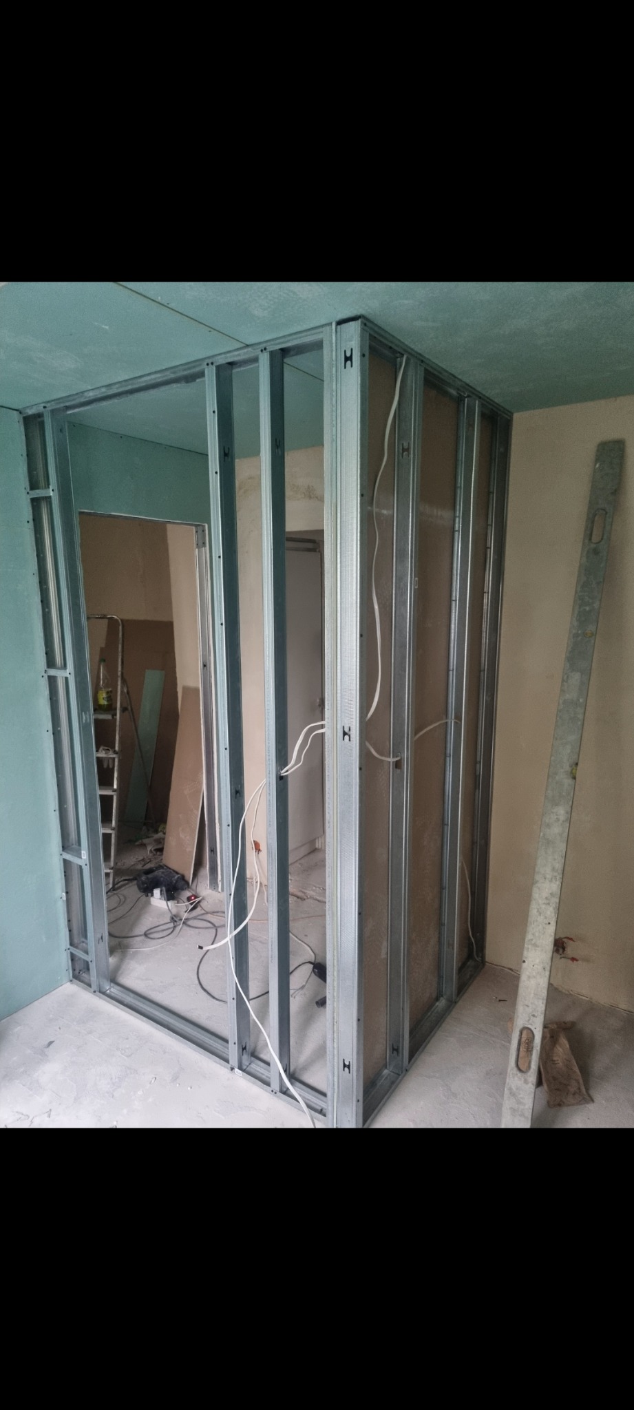 Konstrukcja z metalowych profili do montażu ścianki działowej z płyt gipsowo-kartonowych, widoczne przewody elektryczne, poziomica oparta o ścianę.